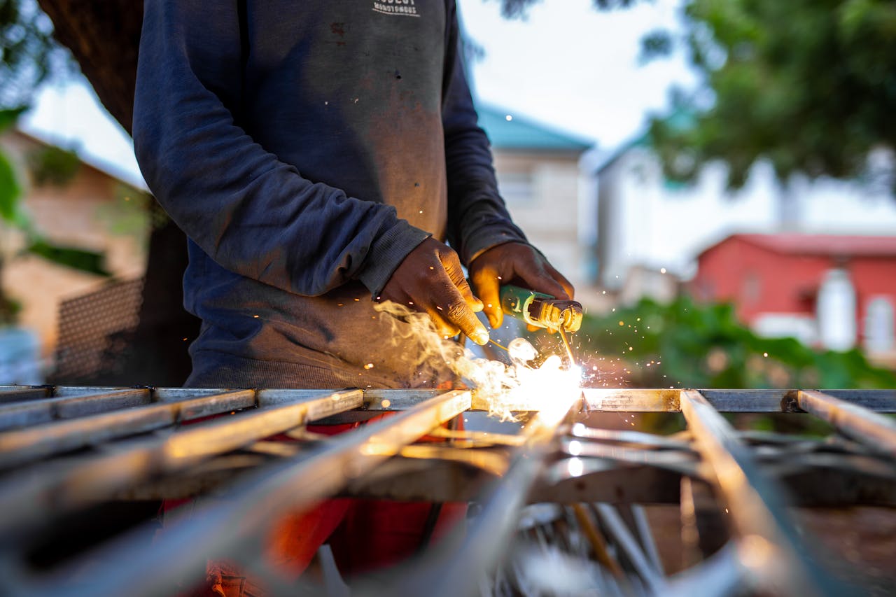 A welder at work outdoors, creating sparks as metal pieces are joined.